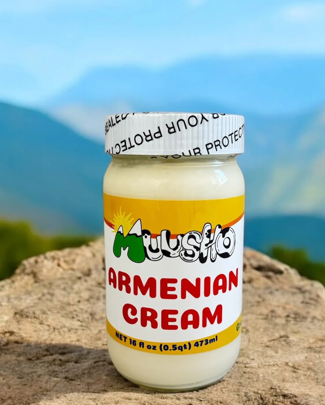 A jar of Muusho Armenian Cream on a sunny rock with blue mountains behind it